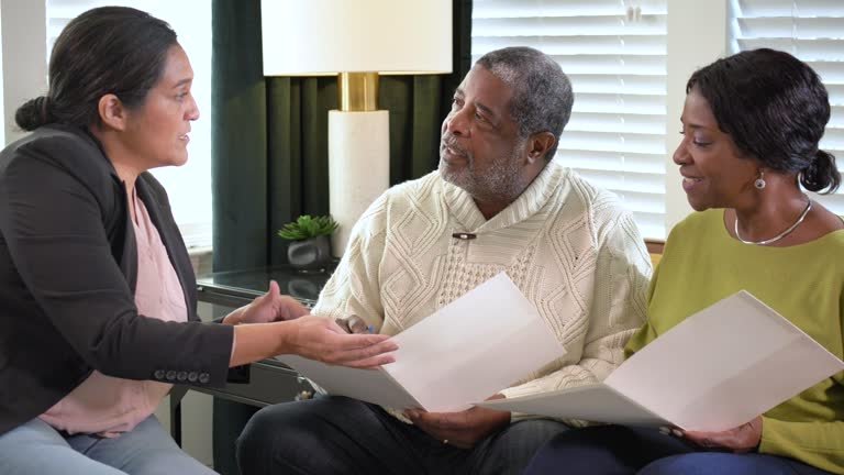 A senior African-American couple meeting with an in-home consultant. The mature Hispanic woman could be a Real Estate Agent, a financial advisor, or insurance agent. They are sitting in the living room getting ready to sign paperwork.